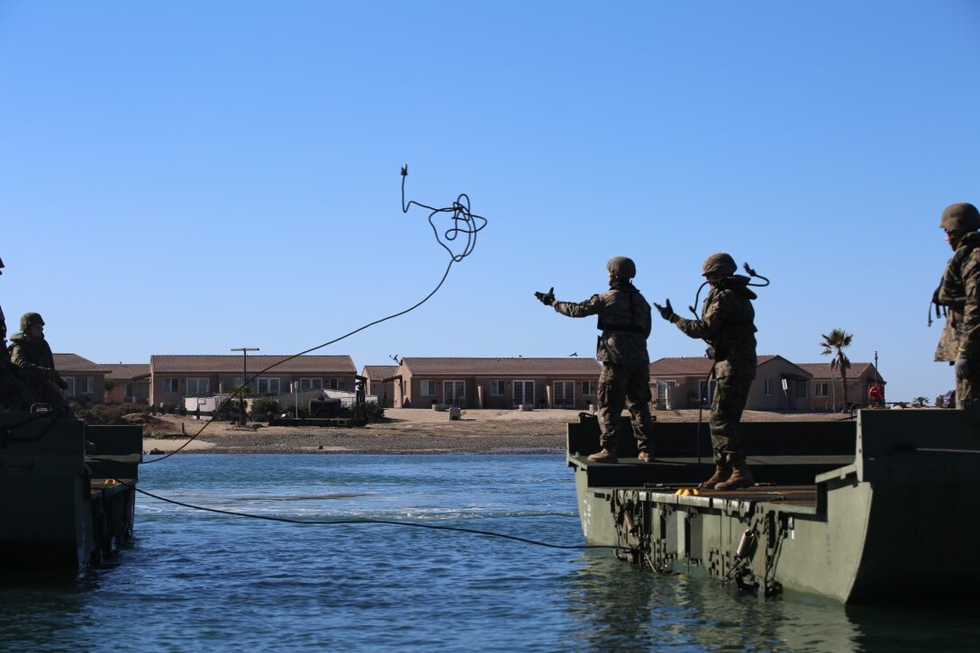 Marines from Bridge Company, 7th Engineer Support Battalion, Combat Logistics Regiment 1, 1st Marine Logistics Group toss lines across a body of water to tow in two Mark III Improved Ribbon Bridges. The battalion trained in tandem with Marines from 6th ESB out of Battle Creek, Mich., aboard Marine Corps Base Camp Pendleton, Dec. 12, 2015. The IRB is a more improved version of the original and is used to move personnel and tactical vehicles over non-passable waterways.