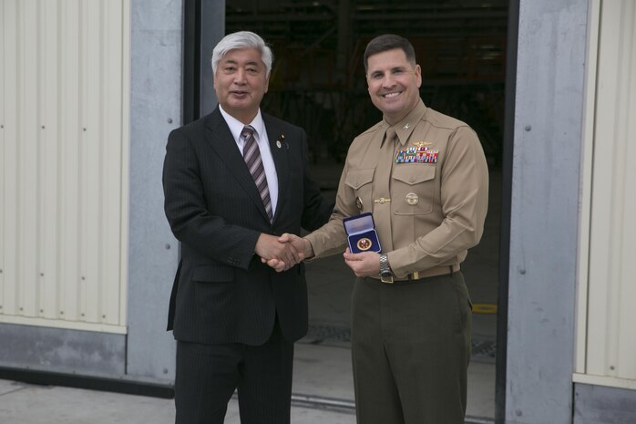 Gen Nakatani, Japanese Defense Minister, presents Col. Robert V. Boucher, commanding officer of Marine Corps Air Station Iwakuni, Japan, with a gift after Nakatani's tour of Marine Aerial Refueler Transport Squadron (VMGR) 152 facilities during his visit to the air station, Dec. 2, 2015. As part of the growing U.S. – Japan relationship, this visit provided Nakatani an opportunity to connect with station officials and view pertinent installation facilities that aid in the Marine Corps’ mission success.