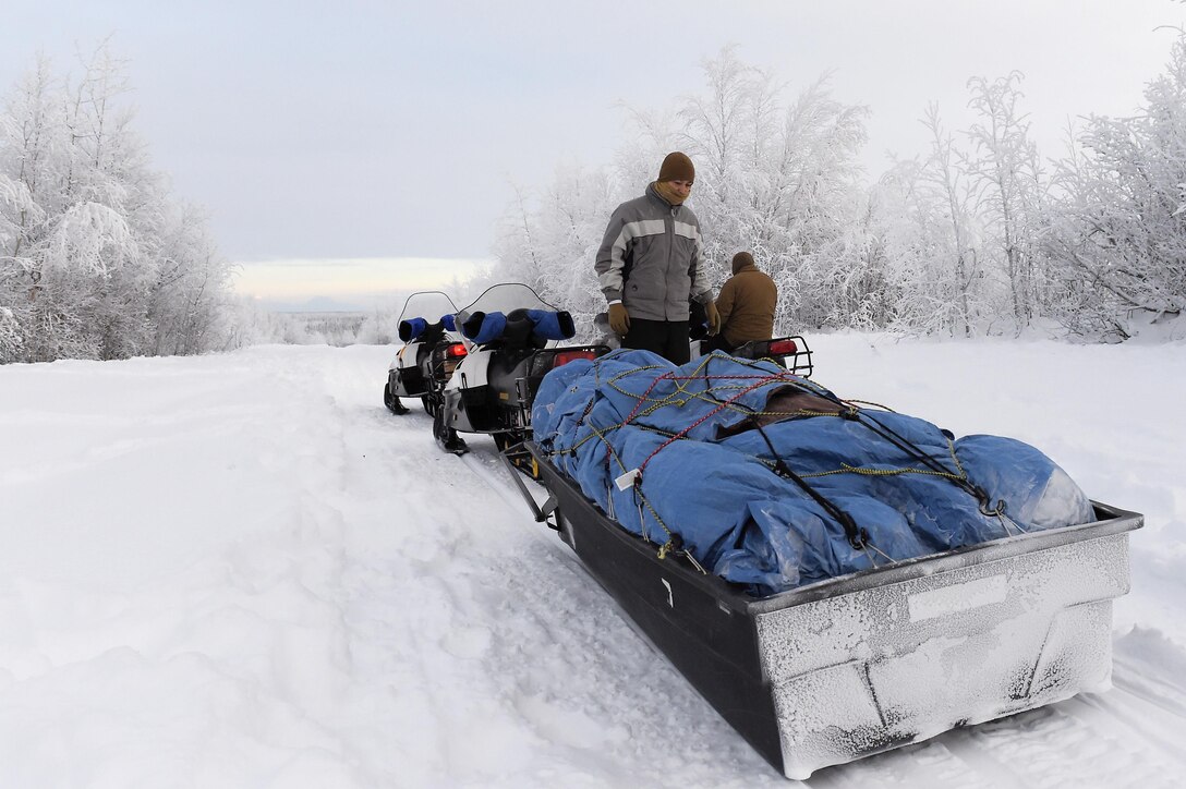 Marine Corps Sgt. Mauricio Sandoval examines his snow mobile and sled filled with gifts while traveling to Nikolai, Alaska, Dec. 11, 2015, to deliver Toys for Tots. Sandoval is assigned to Delta Company, 4th Law Enforcement Battalion. U.S. Air Force photo by Alejandro Pena