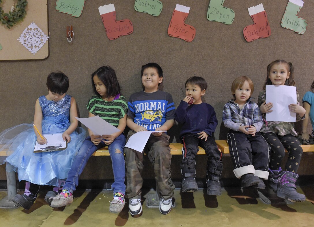 Children hold their their Christmas lists while awaiting toys from Santa Claus, played by Marine Corps Sgt. Mauricio Sandoval, during a Toys for Tots event in Nikolai, Alaska, Dec. 11, 2015. U.S. Air Force photo by Alejandro Pena