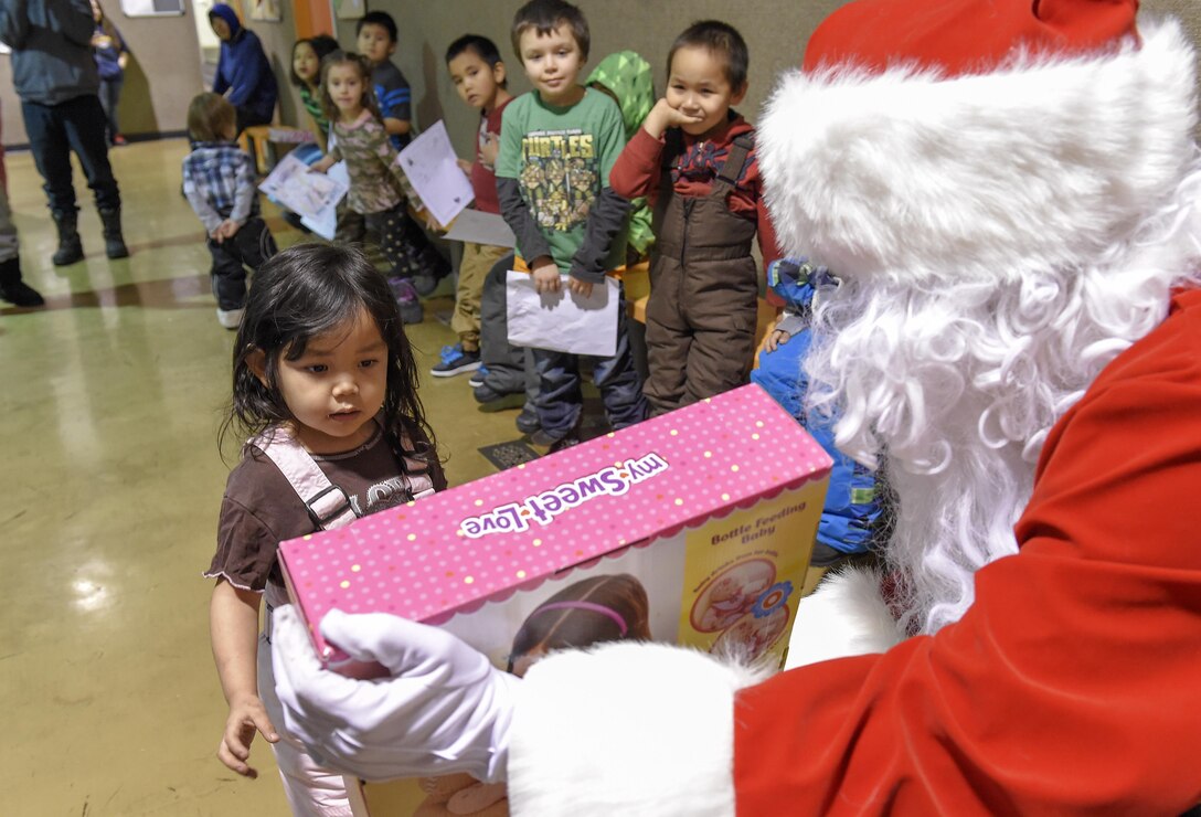 Santa Claus, played by Marine Corps Sgt. Mauricio Sandoval, right, passes out toys to children during a Toys for Tots event at Nikolai, Alaska, Dec. 11, 2015. Sandoval is assigned to Delta Company, 4th Law Enforcement Battalion. U.S. Air Force photo by Alejandro Pena
