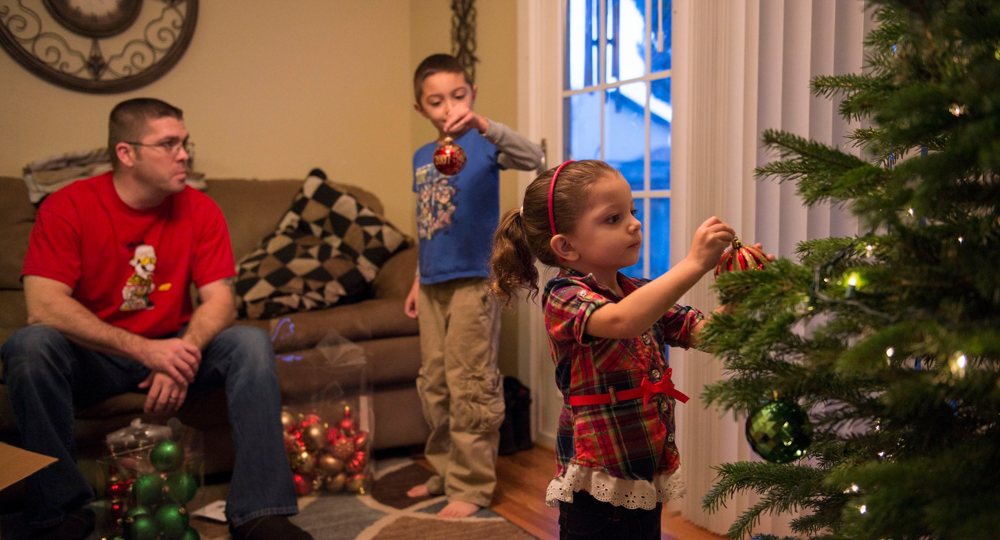 Tech. Sgt. Zachary Payne, 389th Aircraft Maintenance Unit weapons expeditor, watches his son and daughter decorate their family Christmas tree in Mountain Home, Idaho, Dec. 5, 2015. Payne’s wife is currently deployed, so the family sent her a tree of her own to decorate while she's away. (U.S. Air Force photo by Airman 1st Class Jessica H. Evans/RELEASED)