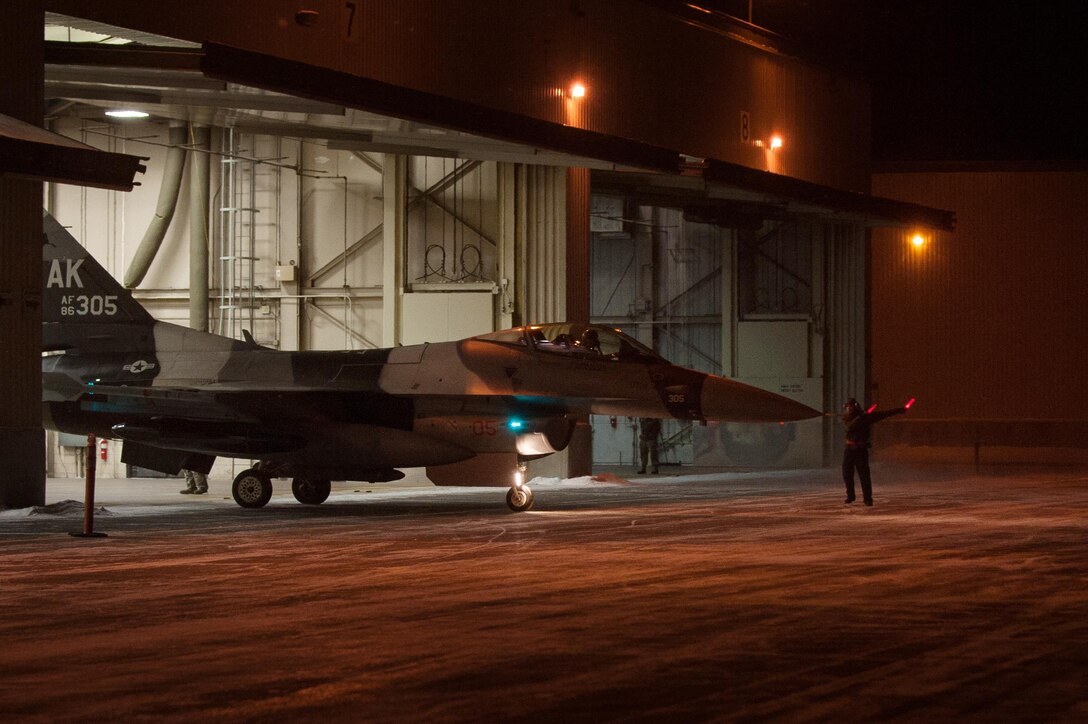 An airman ushers an F-16 Fighting Falcon aircraft out of the bay onto the taxiway on Eielson Air Force Base, Alaska, Dec. 7, 2015. The airman is assigned to the 354th Aircraft Maintenance Squadron. U.S. Air Force photo by Master Sgt. Joseph Swafford