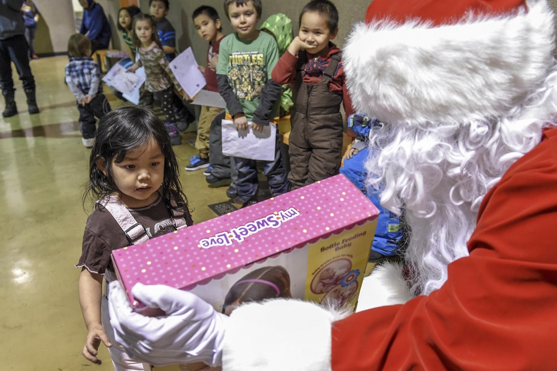 Santa Claus, played by Marine Corps Sgt. Mauricio Sandoval, right, passes out toys to children during a Toys for Tots event at Nikolai, Alaska, Dec. 11, 2015. Sandoval is assigned to Delta Company, 4th Law Enforcement Battalion. Air Force photo by Alejandro Pena 