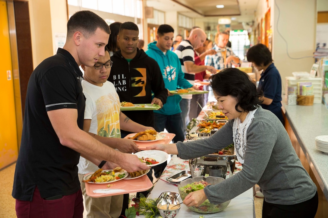 Junko Kurata, right, serves salad to Cpl. Jonathan Koren during a Christmas Party thrown by the Hikariga Oka Nursing Home in Kin Town, Okinawa, Japan, Dec. 18, 2015. The nursing home hosts the Christmas party annually to pay thanks for 7th Communication Battalion continuous contributions and community outreach projects. Since 1994, Marines with the battalion have regularly volunteered regularly by organizing routine cleanups and maintenance for the home and its surrounding area. Kurata is from Kin town and is a nurse at the nursing home. Koren is from Allentown, Pennsylvania and is a digital wideband repairer with 7th Comm. Bn., III Marine Expeditionary Force Headquarters Group, III MEF. (U.S. Marine Corps Photo by Cpl. Devon Tindle/Released)