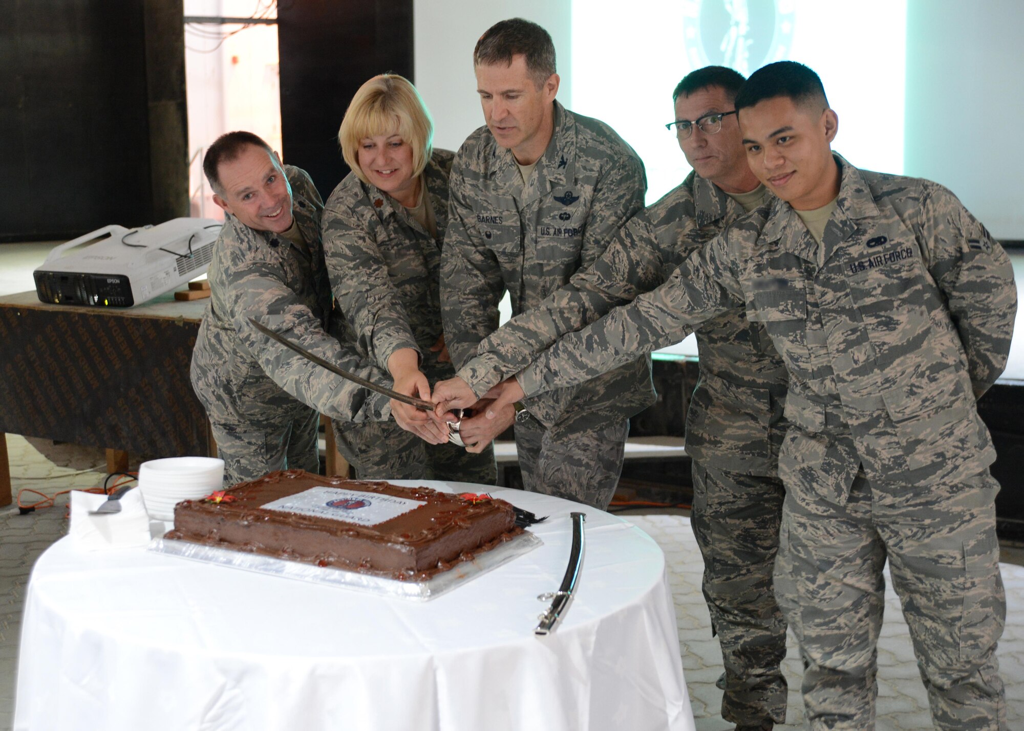 U.S. Air Force Col. Johnny Barnes (center), 380th Air Expeditionary Wing vice commander, prepares to cut a cake with National Guardsmen assigned to the 380th AEW during the National Guard Birthday celebration at an undisclosed location in Southwest Asia, Dec. 12, 2015. Tradition dictated that the youngest and oldest members present have the honor of cutting the birthday cake at National Guard events. (U.S. Air Force photo by Tech. Sgt. Frank Miller/Released)