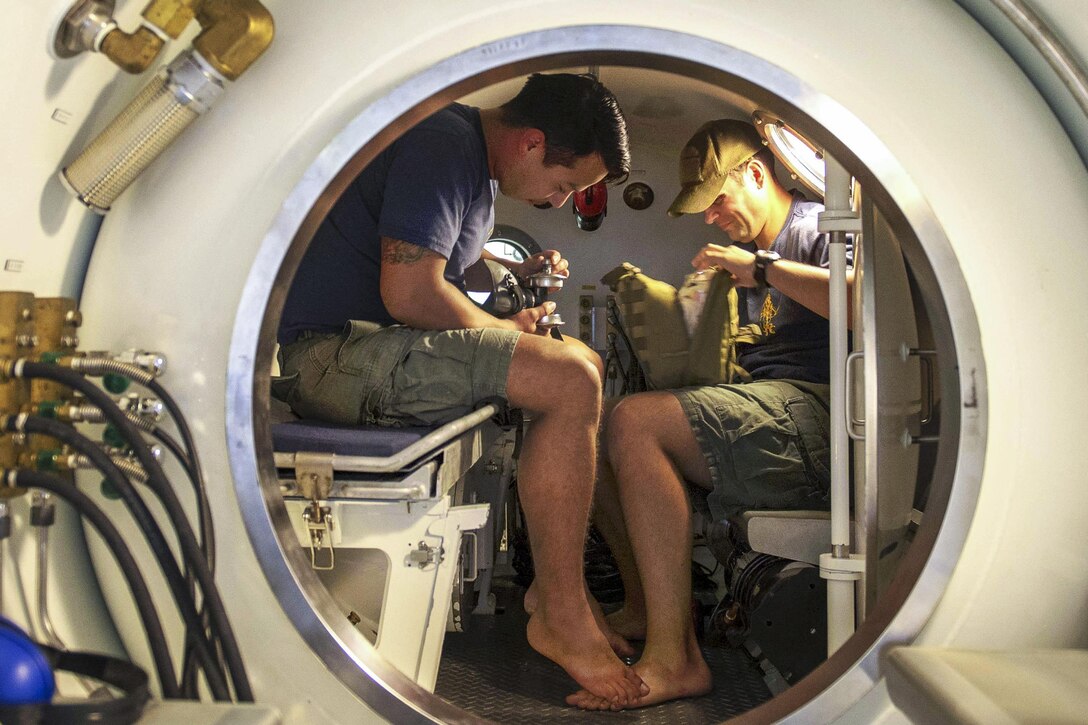 Navy Petty Officers 2nd Class Jonathan Miranda, left, and Ryan McGovern inspect a medical kit inside a double-lock recompression chamber system in Bahrain, Dec. 22, 2015. Miranda is a diver and McGovern is a hospital corpsman. U.S. Navy photo by Petty Officer 2nd Class Shannon Burns