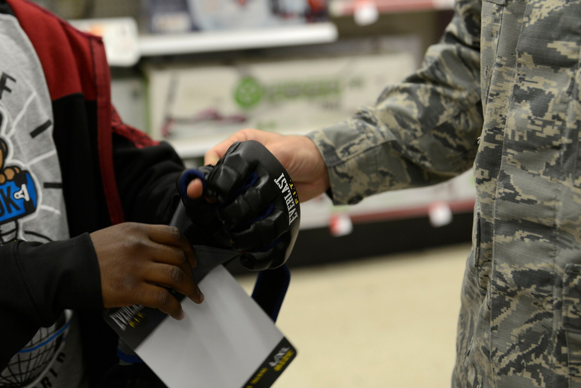 A 20th Security Forces Squadron Airman helps a child from the John K. Crosswell Home for Children, Sumter, S.C., put on an Mixed Martial Arts fighting glove during a Shop with a Cop event at a local store during a Shop with a Cop in Sumter, S.C., Dec. 21, 2015. The children were given $80 to purchase on various toys, clothing, and snacks to share with their families on Christmas morning.  (U.S. Air Force photo by Airman 1st Class Christopher Maldonado)