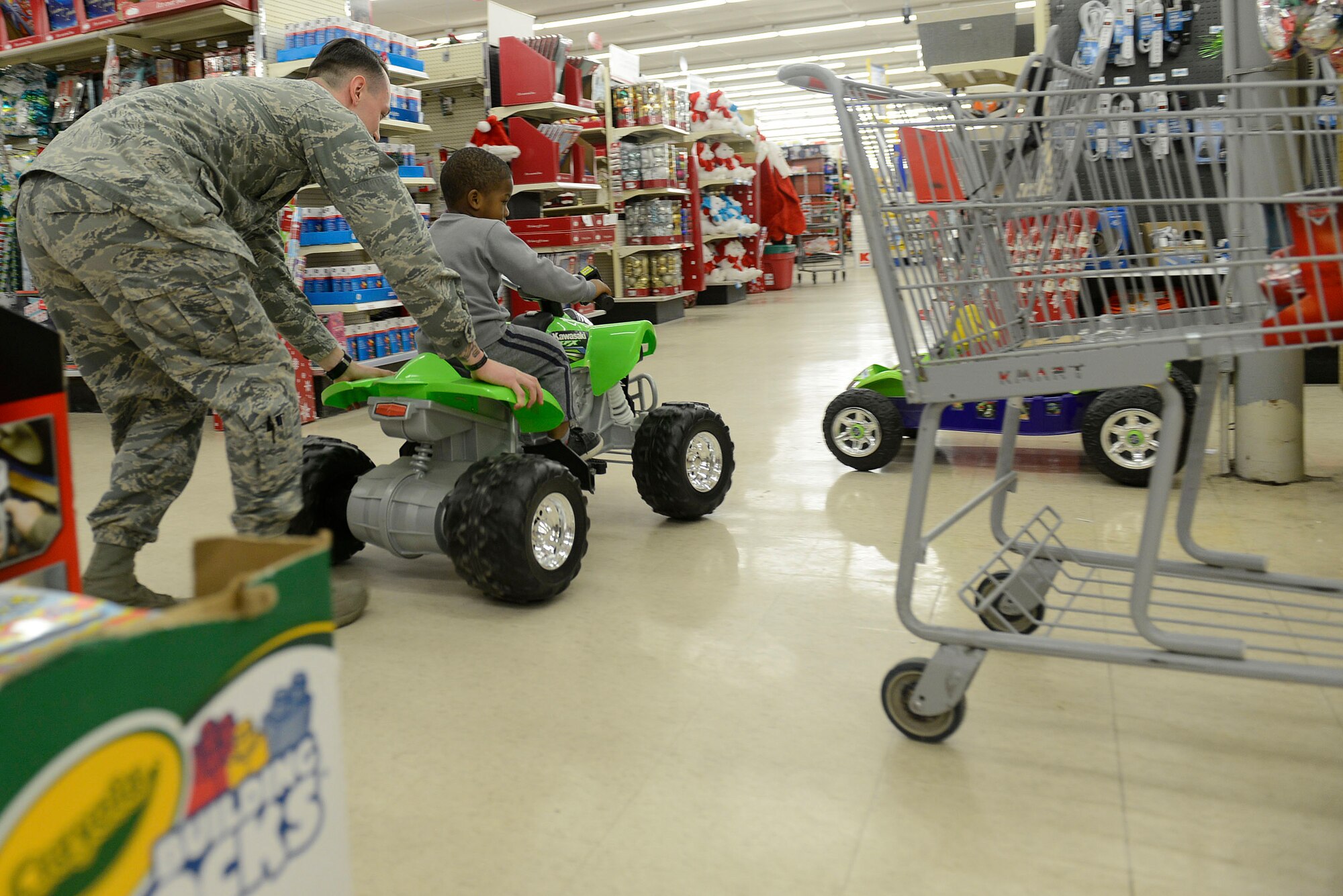 A 20th Security Forces Squadron Airman pushes a child from the John K. Crosswell Home for Children, Sumter, S.C., around a local store in a toy car during a Shop with a Cop event in Sumter, S.C., Dec. 21, 2015. Airmen from the 20th SFS accompanied children as they went Christmas shopping for themselves and family members. (U.S. Air Force photo by Airman 1st Class Christopher Maldonado)