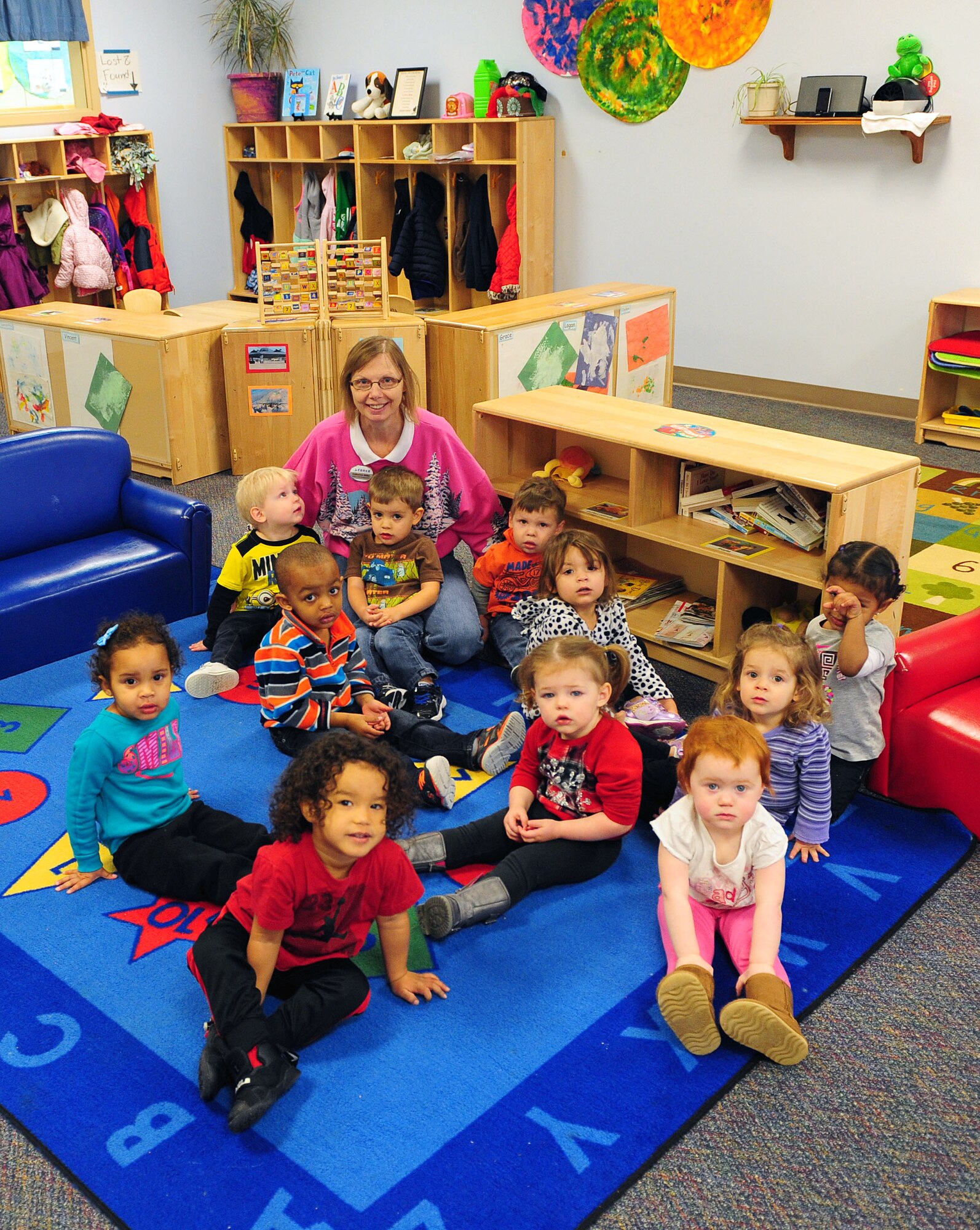 Catherine Miller, a child and youth program assistant with the 509th Force Support Squadron Susie Skelton Child Development Center (CDC), sit with her students prior to story time at Whiteman Air Force Base, Mo., Dec. 22, 2015. In 2010, Miller began a drive to help veterans spending the holiday season alone. This year, 13 different classrooms at the CDC “adopted” a veteran by collecting items and making them cards. (U.S. Air Force photo by Airman 1st Class Jazmin Smith)