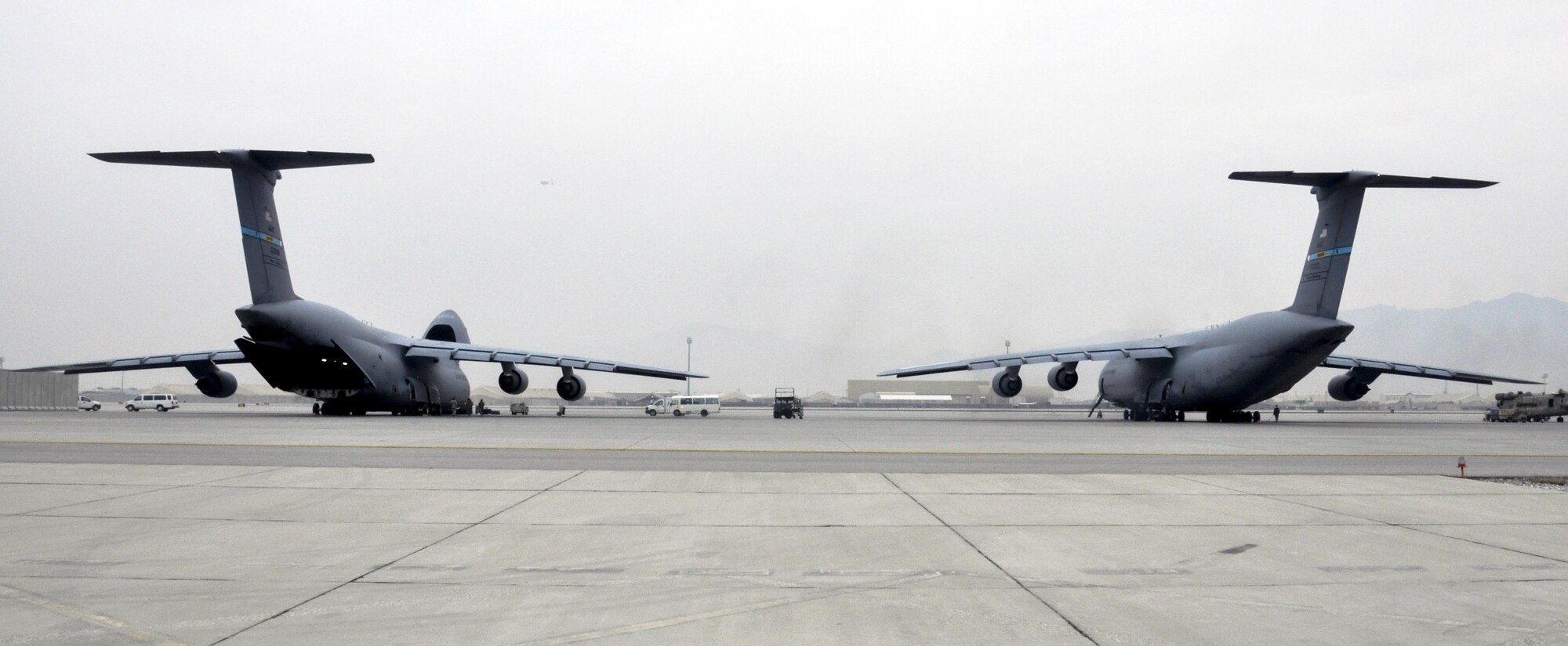 Two C-5M Super Galaxy aircrafts wait while crews from Task Force Destiny and 9th Airlift Squadron, Dover Air Force Base, Del., unload a helicopter at Bagram Airfield, Afghanistan Dec. 26, 2015. The C-5M is the largest military transport aircraft in the world, capable of hauling 270,000 pounds of cargo. (U.S. Air Force photo by Tech. Sgt. Nicholas Rau) 