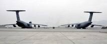 Two C-5M Super Galaxy aircrafts wait while crews from Task Force Destiny and 9th Airlift Squadron, Dover Air Force Base, Del., unload a helicopter at Bagram Airfield, Afghanistan Dec. 26, 2015. The C-5M is the largest military transport aircraft in the world, capable of hauling 270,000 pounds of cargo. (U.S. Air Force photo by Tech. Sgt. Nicholas Rau) 