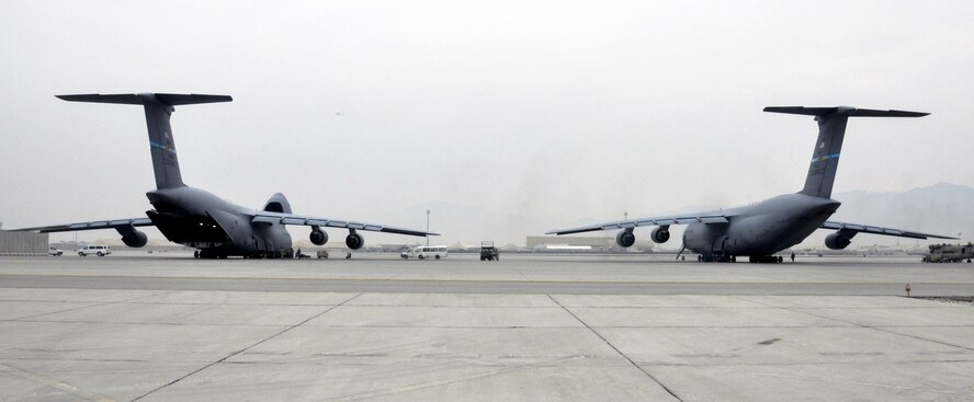 Two C-5M Super Galaxy aircrafts wait while crews from Task Force Destiny and 9th Airlift Squadron, Dover Air Force Base, Del., unload a helicopter at Bagram Airfield, Afghanistan Dec. 26, 2015. The C-5M is the largest military transport aircraft in the world, capable of hauling 270,000 pounds of cargo. (U.S. Air Force photo by Tech. Sgt. Nicholas Rau) 