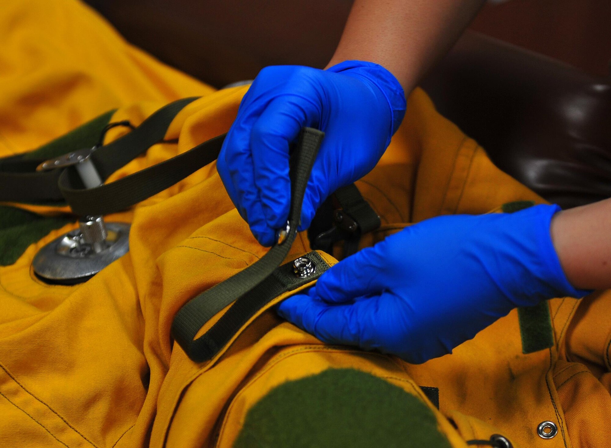 A 99th Expeditionary Reconnaissance Squadron physiological support technician closes a button clasp on a full-pressure suit at an undisclosed location in Southwest Asia, Dec. 22, 2015. Technicians inspect the suits, fastening all their buttons and Velcro patches to prevent the suit’s material from fraying after taking them off pilots. (U.S. Air Force photo by Staff Sgt. Kentavist P. Brackin/released)