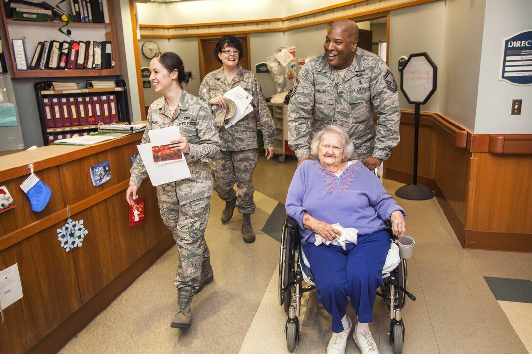 U.S. Air Force Senior Master Sgt. Harry Waugh, right, wheels a patient while airmen sing along with fourth graders from the Seaview School in Linwood, N.J., during the 15th Annual Holiday "Songfest" at the New Jersey Veterans Memorial Home at Vineland, N.J., Dec. 16, 2015. Waugh is assigned to the New Jersey Air National Guard’s 177th Fighter Wing. New Jersey Air National Guard photo by Master Sgt. Mark C. Olsen