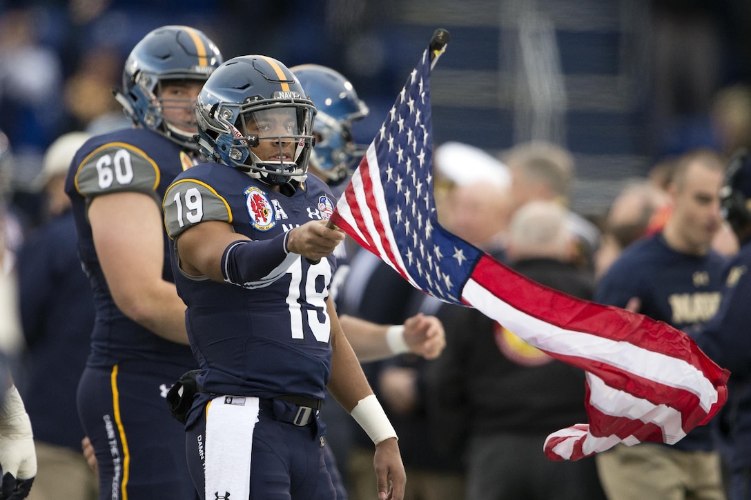 Midshipman Keenan Reynolds, the U.S. Naval Academy quarterback, holds the American flag as Navy enters Navy-Marine Corps Memorial Stadium for the the 2015 Military Bowl in Annapolis, Md., Dec. 28, 2015. Reynolds broke the NCAA Football Bowl Subdivision record for touchdowns with 88 and also set the career rushing yards with 4,559 yards. DoD News photo by EJ Hersom