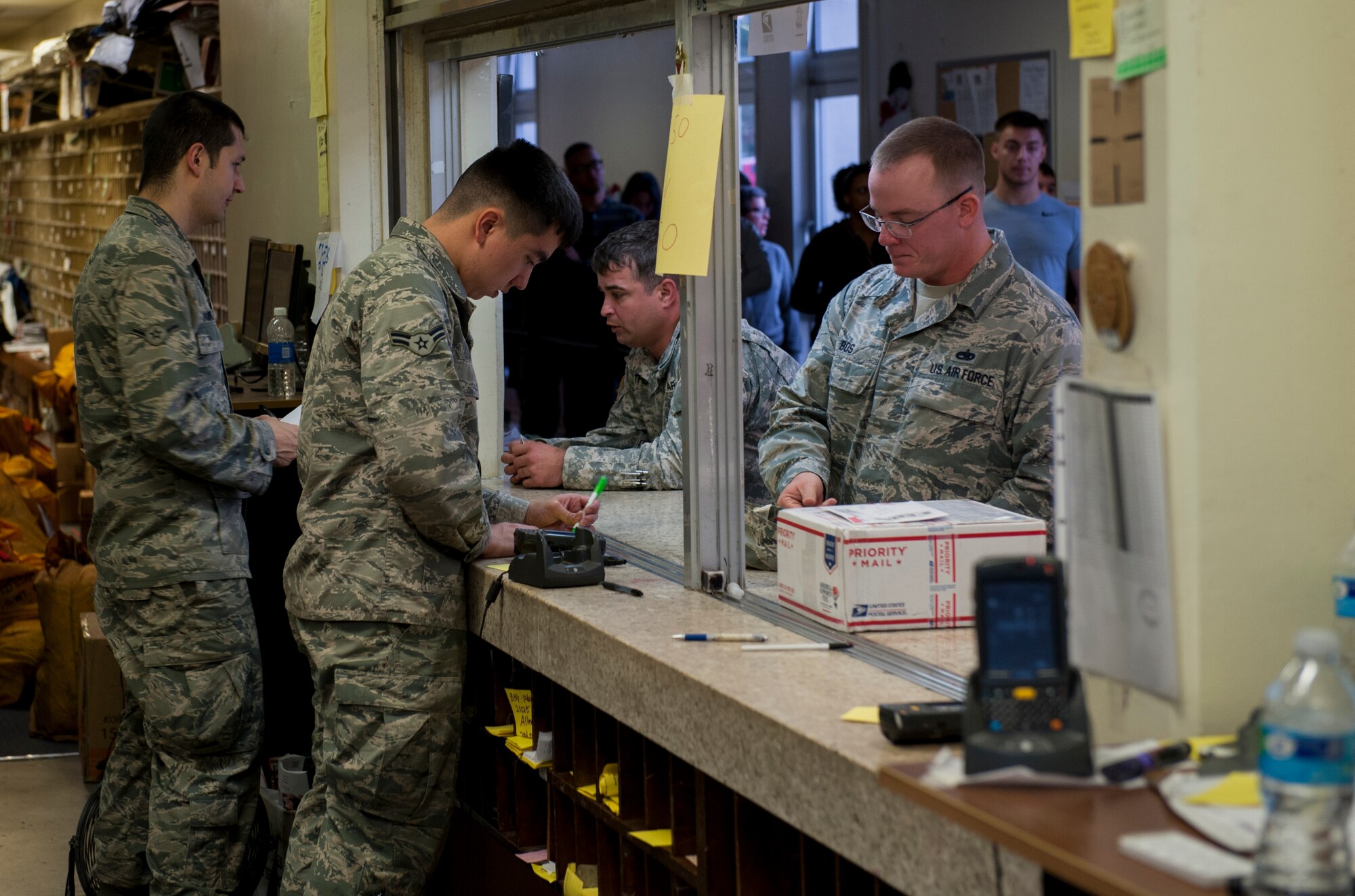 Two U.S. Air Force Airmen working for the Kadena Post Office assist customers, Dec. 30, 2015, at Kadena Air Base, Japan. The post office delivers approximately 3 million pounds of mail a year and provides service for 27,000 customers on Okinawa. (U.S. Air Force photo by Airman Zackary A. Henry)