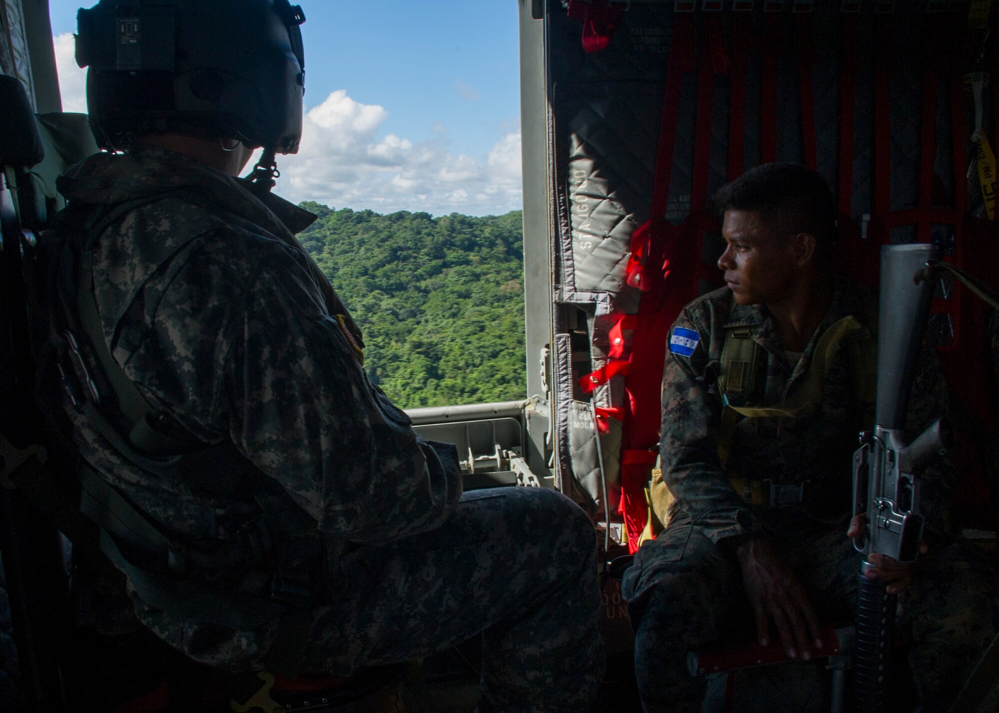 David Uplinger 1-228th Aviation Regiment flight engineer and a Honduran troop watch the trees slip by the door of a U.S. Army CH-47 Chinook Dec. 17, 2015, as they fly over the Gracias a Dios Department (state) of Honduras. The airlift for the troops is a result of a request for assistance to help disrupt the flow of drugs in the region by the Honduran president in October 2014. (U.S. Air Force photo by Capt. Christopher Mesnard/Released)