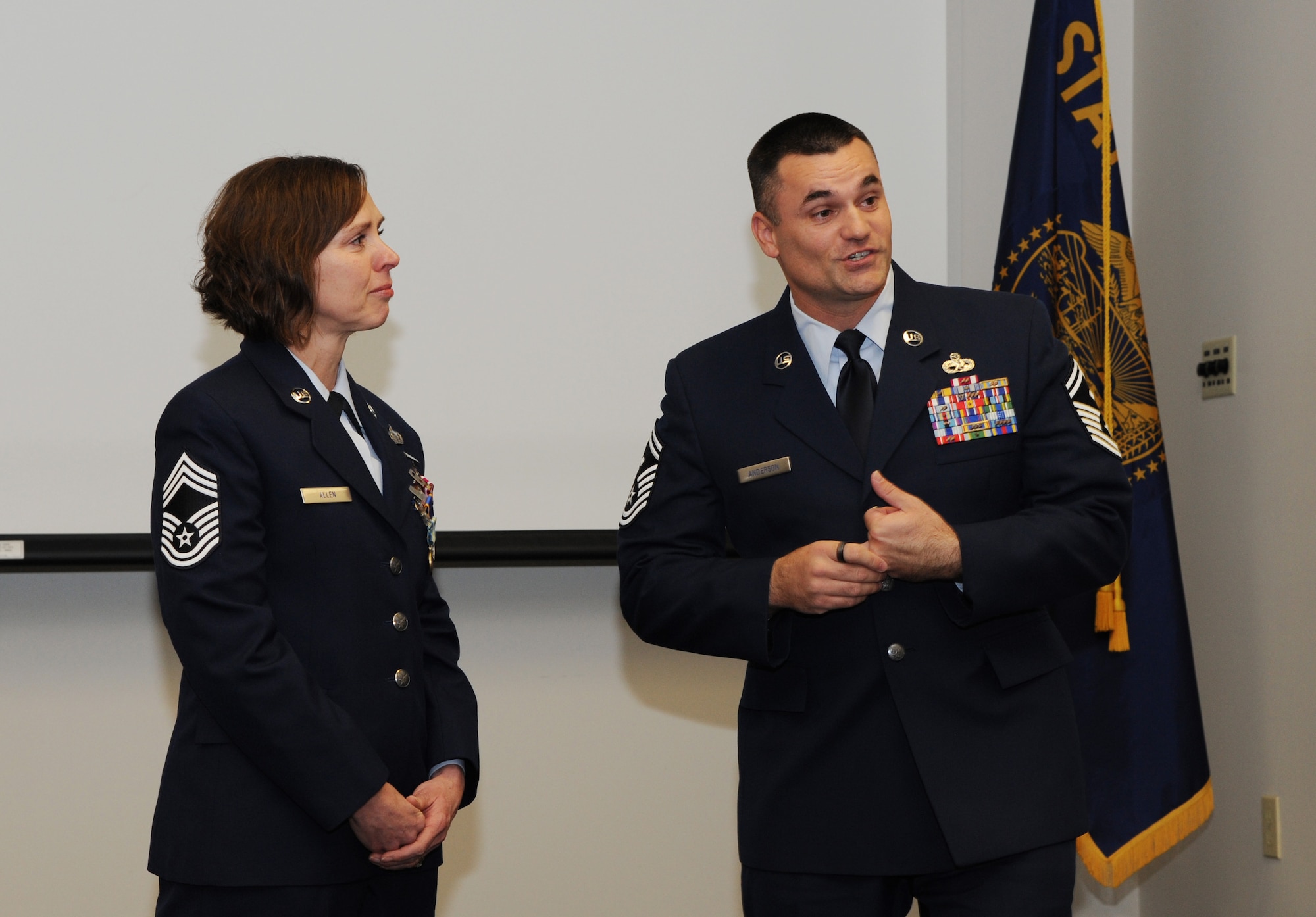 Chief Master Sgt. Jean Allen, left, listens to her son, Air Force Senior Master Sgt. Jason Anderson, right, address those attending her retirement ceremony, Dec. 22, 2015, Portland Air National Guard Base, Ore. (Air National Guard photo by Tech. Sgt. John Hughel, 142nd Fighter Wing Public Affairs)