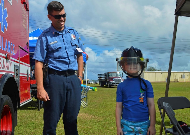 SANTA RITA, Guam (Dec. 19, 2015) Captain Douglas Kelly from the Navy Fire and Emergency Services on Naval Base Guam helps a child dawn a firefighting helmet during the first ever Team 15 Day event December 19.  Team 15 Day, hosted by Submarine Squadron 15, is an event that brings together Sailors and families from the submarine community on Guam to educate them on Navy support services and acclimate new arrivals to life on Guam.