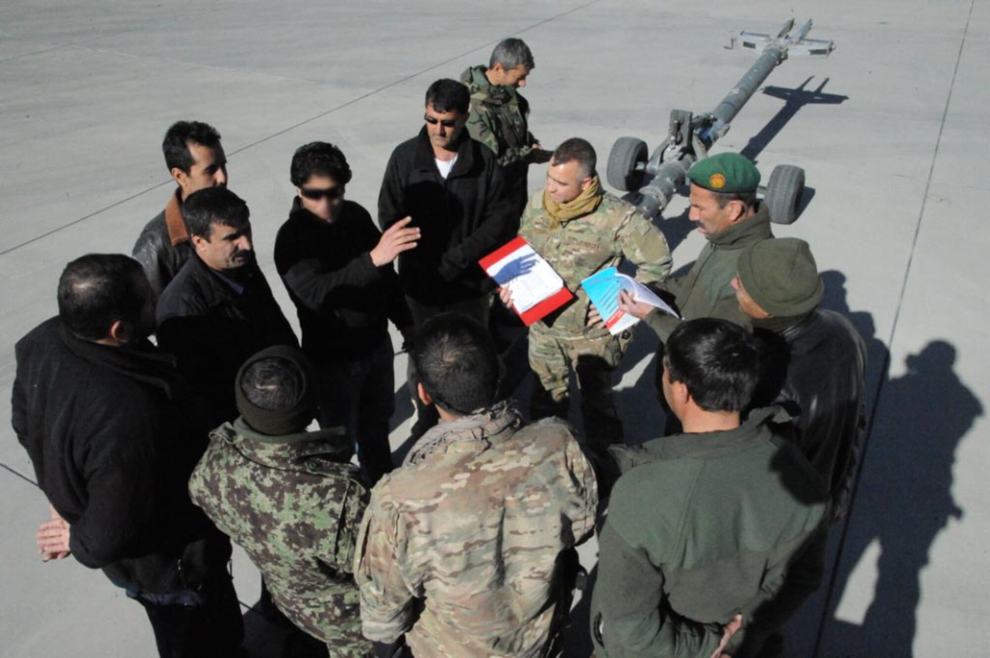 Afghan C-130 maintainers gather around Senior Airman Irwin Rodriguez, Train, Advise, Assist Command-Air fixed wing advisor to learn the proper way to connect a tow bar to a C-130. Afghans are now participating in C-130 maintenance lead-in training to better prepare them for formal training. The ability to maintain their own aircraft without coalition support is another step toward a completely independent Afghan Air Force. (US Air Force photo by Senior Master Sgt. J. LaVoie/Released) (Face blurred for security)