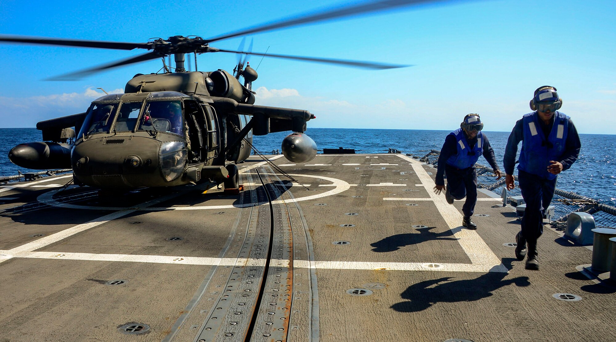 U.S. Navy plane handlers leave the rotor area after tying down a UH-60 Blackhawk helicopter assigned to the 1st Battalion, 228th Aviation Regiment during deck landing qualifications off the coast of Honduras, Feb. 1, 2015.  The 1-228th Avn. Reg. aircrew participated in deck landing qualifications on board the USS Kauffman to qualify pilots and crew chiefs on shipboard operations.  Kauffman is on its final scheduled deployment to the U.S. Southern Command area of responsibility supporting multinational, counter-narcotics operation known as Operation Martillo. (U.S. Air Force photo/Tech. Sgt. Heather Redman)