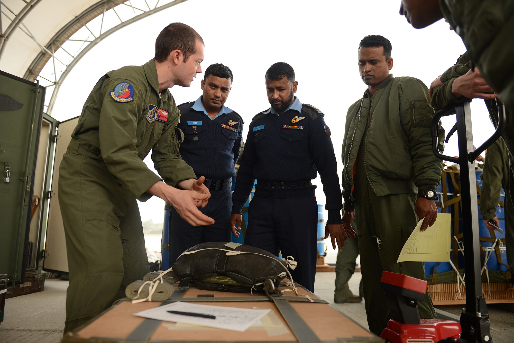 U.S. Air Force Tech. Sgt. Chris Nichols (left) speaks with Bangladesh Air Force personnel from the 101st Special Flying Unit about low-cost, low-altitude airdrop bundle rigging inspection procedures during a subject matter expert exchange at Exercise COPE NORTH, BAF Base Bangabandhu, Jan. 27, 2015. Nichols is an instructor loadmaster assigned to the 374th Operations Support Squadron, Yokota Air Base, Japan. COPE SOUTH is a Pacific Air Forces-sponsored, bilateral tactical airlift exercise conducted in Bangladesh, with a focus on cooperative flight operations, day and night low-level navigation, tactical airdrop, and air-land missions as well as subject-matter expert exchanges in the fields of operations, maintenance and rigging disciplines. COPE SOUTH helps cultivate common bonds, foster goodwill, and improve readiness and compatibility between members of the Bangladesh and U.S. Air Forces. (U.S. Air Force photo by 1st Lt. Jake Bailey/Released)