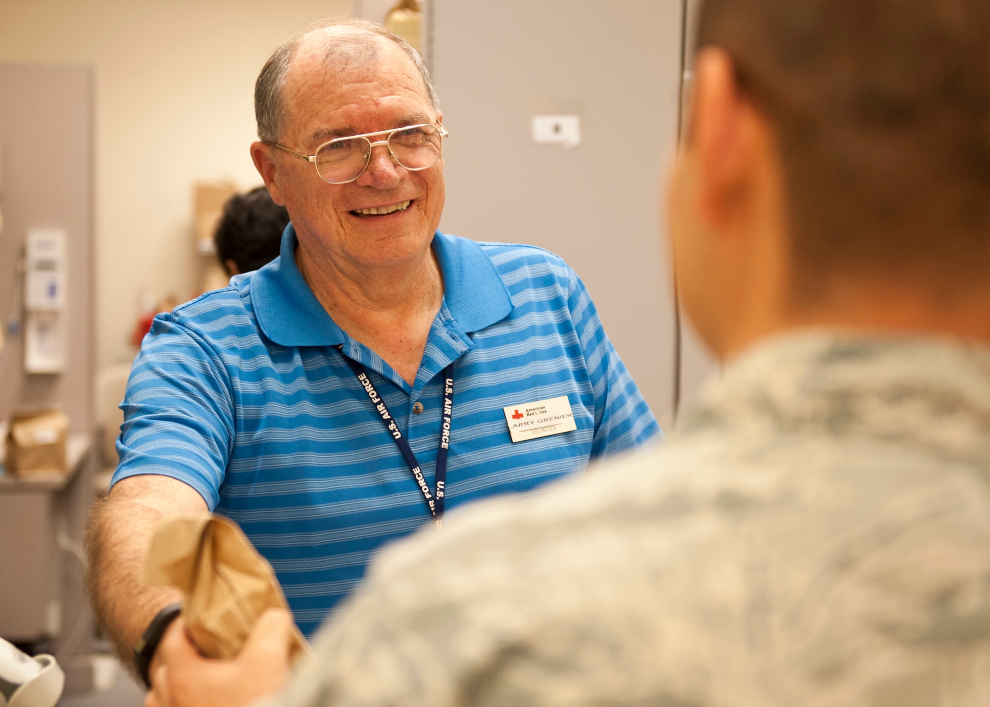 PETERSON AIR FORCE BASE, Colo. – Larry Grenier, American Red Cross volunteer, hands a customer their medication at the Pharmacy East located at the Base Exchange and Commissary complex, Jan. 29, 2015. Grenier has been working with the Red Cross at the pharmacy since August 2008, shortly after he retired from the Air Force. Red Cross volunteers mainly work at the two pharmacies on Team Pete to help with the busy work flow of customers and their fellow co-workers. (U.S. Air Force photo by Senior Airman Tiffany DeNault)