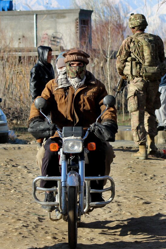 An Afghan man riding a motorcycle passes U.S., Czech and Afghan soldiers as they patrol through a village in Parwan province, Afghanistan, Jan. 26, 2015.