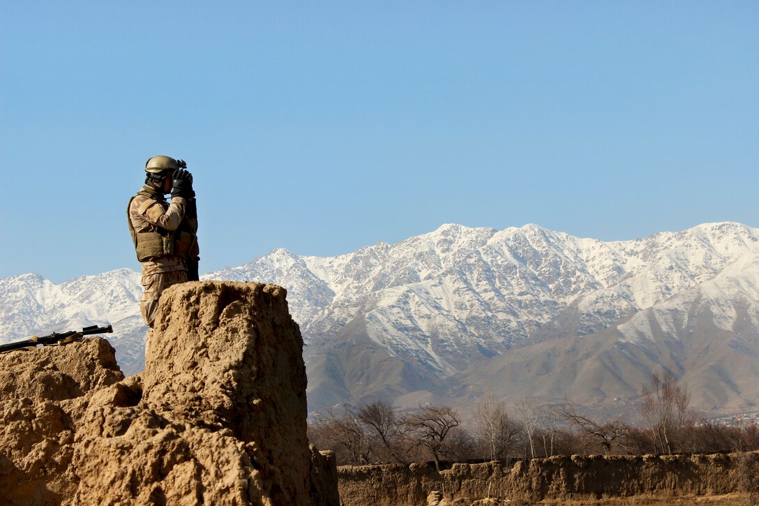 A Czech soldier scans the area using binoculars while providing security from behind a partial stone wall during a patrol with U.S. and Afghan soldiers through a village in Parwan province, Afghanistan, Jan. 27, 2015.