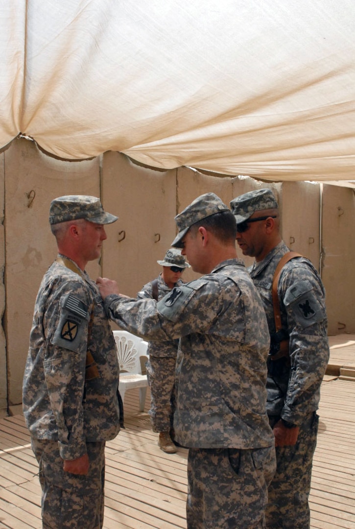 The 2nd Battalion, 156th Infantry Regiment Commander Lt. Col. Eric "Clay" Rivers awards Sgt. 1st Class Timothy Champagne with an Army Commendation Medal with V device five years after the fact for his actions, March 10, 2005, in support of Operation Iraqi Freedom III, as Battalion Command Sgt. Maj. Sud Robertson witnesses. The 2-156th is currently deployed with the Louisiana National Guard's 256th Infantry Brigade Combat Team to set the conditions for the responsible drawdown of U.S. armed forces and equipment in Iraq.