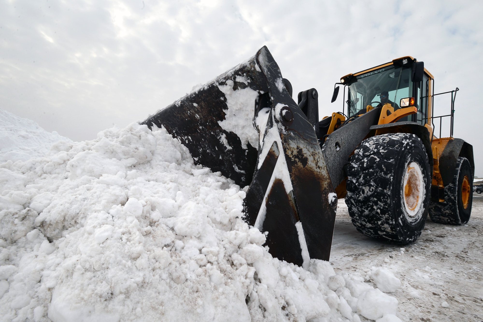Members of the 66th Civil Engineering Division snow removal team removes snow from the Army and Air Force Exchange Service parking lot Feb. 4 after several more inches of snow dropped during the latest winter storm to hit the region. The base has received more than three feet of snow over the past two storms. (U.S. Air Force photo by Jerry Saslav)