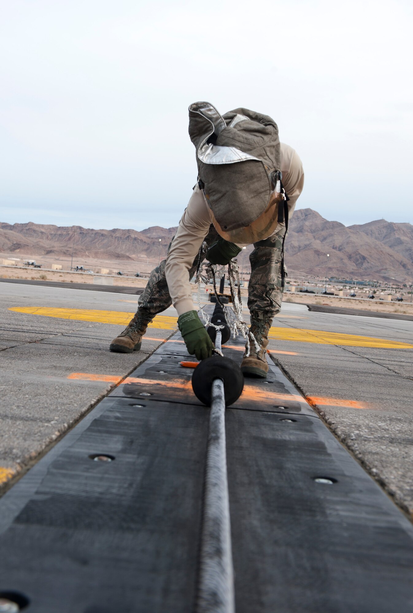 Staff Sgt. Brian Wernet, 99th Civil Engineer Squadron fire protection craftsman, removes ropes securing a barrier from the runway during Red Flag 15-1 to allow large aircraft to land at Nellis Air Force Base, Nev., Jan. 28, 2015. The barrier allows jets to grab a secured line via a tail hook as a last resort if they are unable to stop under their own power. (U.S. Air Force photo by Staff Sgt. Victoria Sneed)