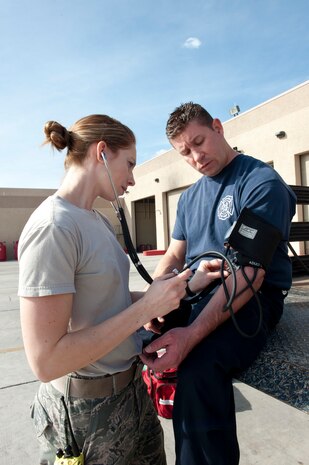 Senior Airman Marissa Henderson, 99th Civil Engineer Squadron fire protection journeyman, practices taking blood pressure on Mike Persall, 99th Civil Engineer Squadron driver and operator, at Nellis Air Force Base, Nev., Jan. 28, 2015. Fire fighters are emergency medical responders who can provide life-saving care in emergency situations. (U.S. Air Force photo by Staff Sgt. Victoria Sneed)