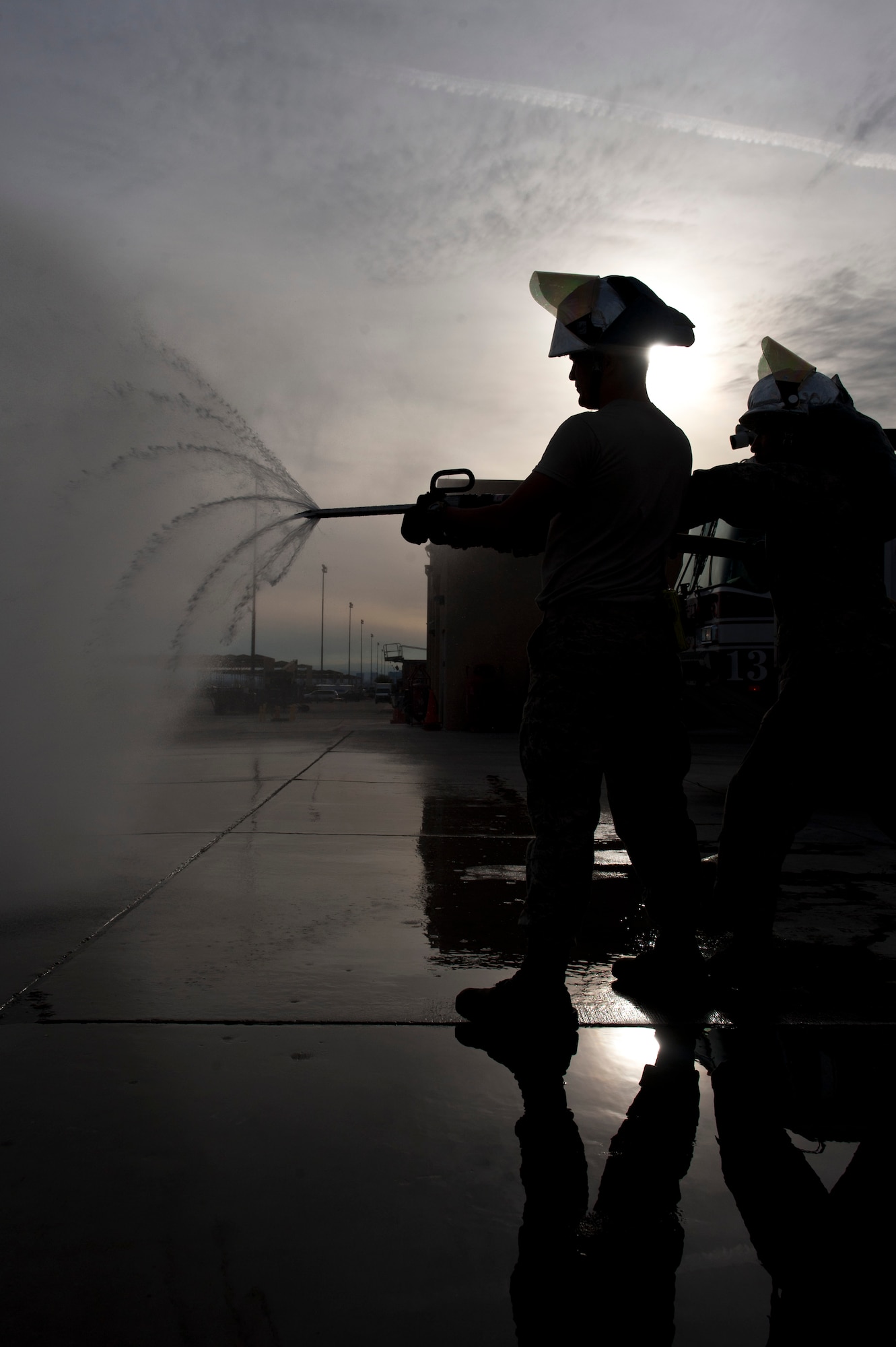 Airmen 1st Class Paul Floyd and Lyndon Martinez, 99th Civil Engineer Squadron fire protection apprentices, spray water from a fire drill during training at Nellis Air Force Base, Nev., Jan. 28, 2015. The drill is used to pierce the skin of an aircraft allowing water to suppress internal fires that are not easily accessed. (U.S. Air Force photo by Staff Sgt. Victoria Sneed)