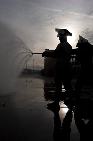 Airmen 1st Class Paul Floyd and Lyndon Martinez, 99th Civil Engineer Squadron fire protection apprentices, spray water from a fire drill during training at Nellis Air Force Base, Nev., Jan. 28, 2015. The drill is used to pierce the skin of an aircraft allowing water to suppress internal fires that are not easily accessed. (U.S. Air Force photo by Staff Sgt. Victoria Sneed)