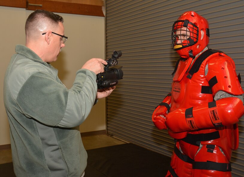 The noncommissioned officer in charge of public affairs at the 932nd Airlift Wing, Tech. Sgt. Christopher Parr, sets his cinematic camera to capture the right lighting conditions indoors as the commander, Col. Karl Goerke, dressed up in the protective "red man" fighting suit.  This was just moments before the leader of the wing helped security forces train with some live fighting action at the unit in Illinois.  (U.S. Air Force photo/Staff Sergeant Amber Hodges)