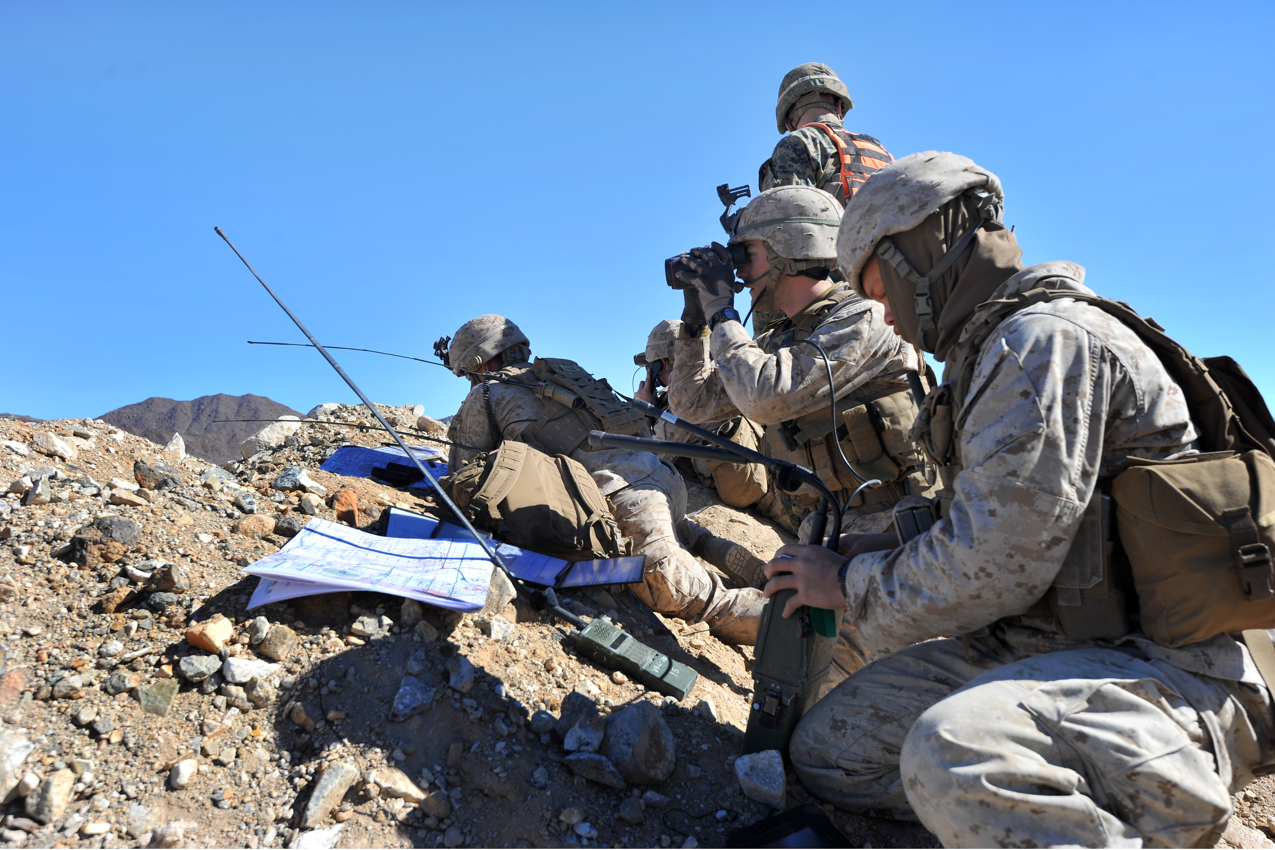 A Marine scans the area using binoculars as other Marines look over a