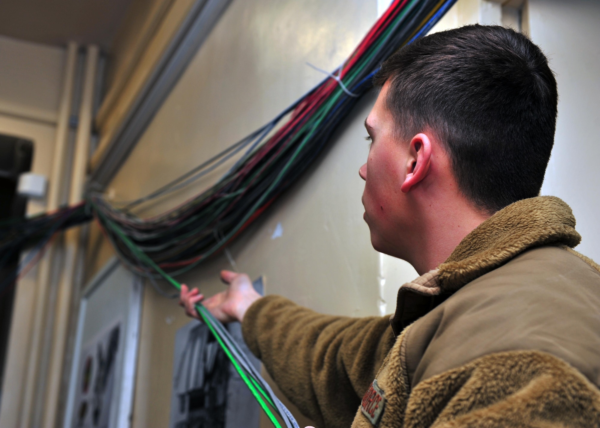 U.S. Air Force Senior Airman James Jarvis, 85th Engineering and Installation Squadron cable and antenna technician, gathers cables prior to feeding them through network cable paths as part of a rewiring project Jan. 28, 2015 at Bagram Airfield, Afghanistan. The project, scheduled to take 100 days to complete, will ensure Emissions Security requirements are upheld and prevent secure information from being leaked through emanation. (U.S. Air Force photo by Staff Sgt. Whitney Amstutz/released)