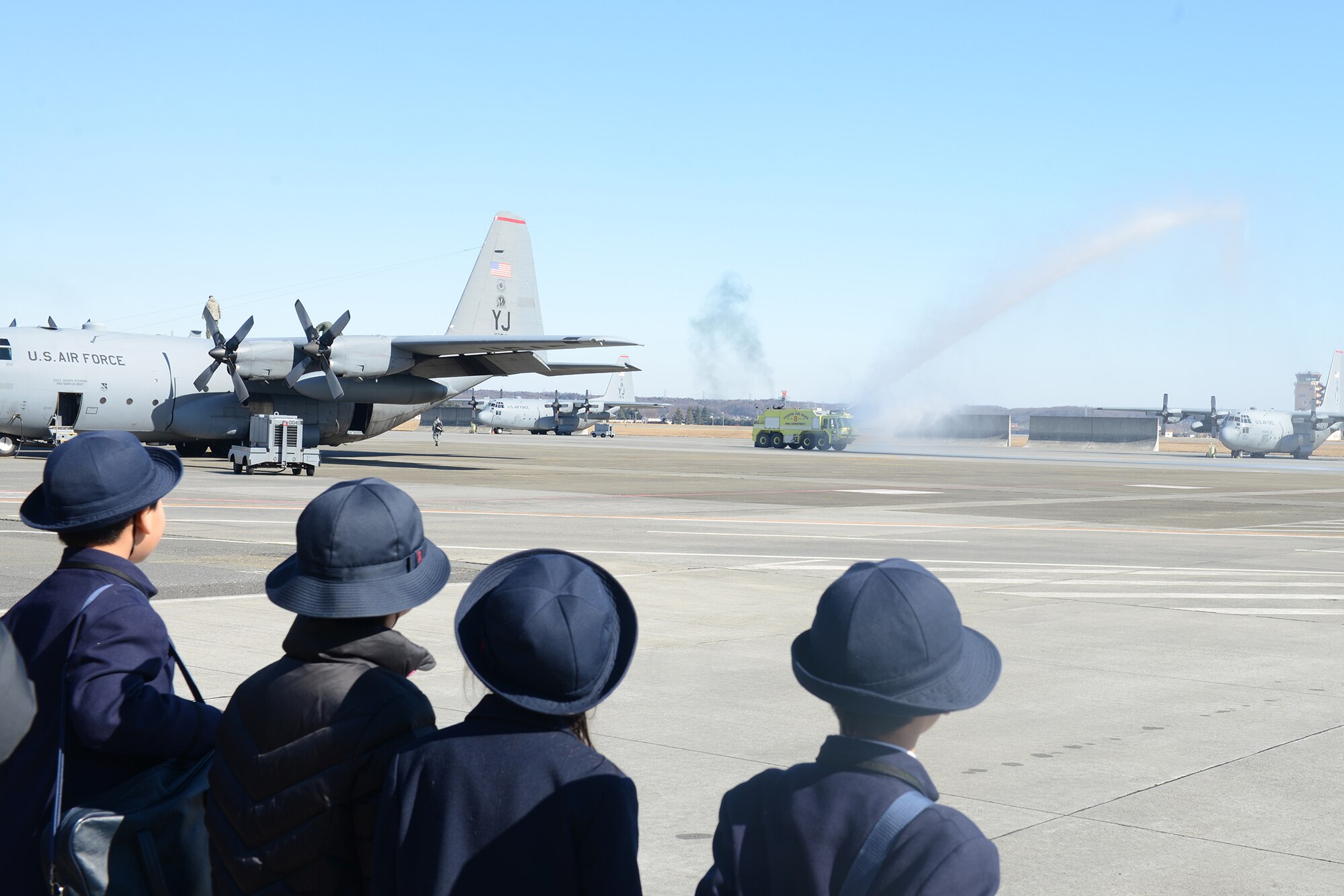 Students from Keimei Gakuen watch as a 374th Civil Engineer Squadron crash rig sprays water across the flightline at Yokota Air Base, Japan, Feb. 3, 2015. These rigs typically carry payloads of more than 3,000 gallons of water used to put out emergency aircraft fires. (U.S. Air Force photo by Airman 1st Class David C. Danford/Released)