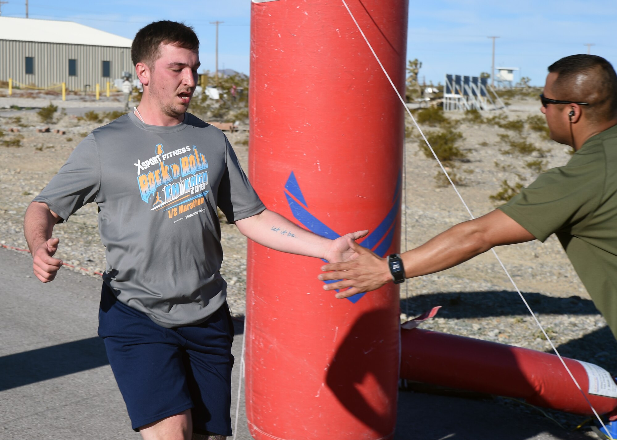 Senior Airman Roger Murvin, left, 99th Ground Combat Training Squadron base security operation instructor, receives a congratulatory handshake from Master Sgt. Dzajic Martinez, right, 99 GCTS NCOIC of operations, as he crosses the finish line of a 5K run Feb. 4, 2014 at Silver Flag Alpha training range.  For nearly 20 years 99th GCTS instructors have prepared thousands of Airmen for combat using the Silver Flag Alpha training range located south of Creech Air Force Base, Nevada and were the first to receive the Air Combat Command Order of the Shield award for their efforts. (U.S. Air Force Photo/Tech. Sgt. Shad Eidson/Released)
