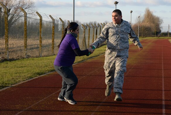 U.S. Air Force Staff Sgt. Raul Sierra, right, 100th Force Support Squadron fitness specialist from Atlantic City, N.J., passes a baton to a Team Mildenhall member during a relay race Feb. 6, 2015, at Heritage Park on RAF Mildenhall, England. The relay race was held as the first competition for the Biggest Loser program hosted by the 100th FSS. (U.S. Air Force photo by Airman 1st Class Jonathan Light/Released)