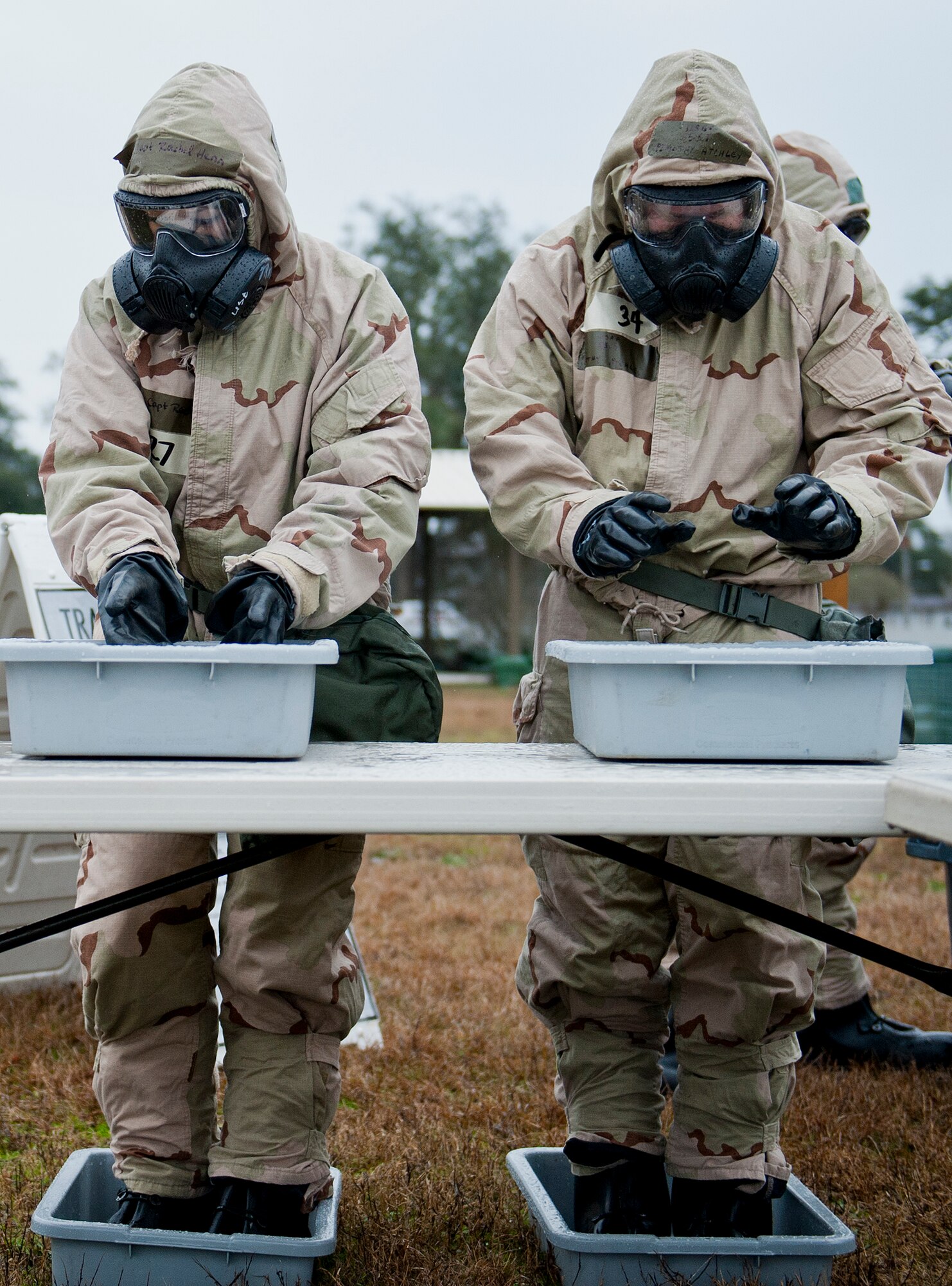 Capt. Rachel Henn, of the 96th Medical Operations Squadron and Staff Sgt. Timothy Atchley, of the 96th Logistics Readiness Squadron, rinse their protective gloves and boots in a simulated bleach solution during a rainy Phase II readiness exercise Feb. 4 at Eglin Air Force Base, Fla.  A Phase II evaluates an Airman’s ability to meet wartime and contingency taskings of employing and sustaining the force and the ability to survive and operate. More than 30 potential deployers received classroom and practical field training during the exercise. (U.S. Air Force photo/Ilka Cole)