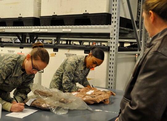 From left, Airman 1st Class Kelsey Williams, 627th Logistics Readiness Squadron flight service center apprentice, and Airman 1st Class Victoria Montgomery, 446th Logistics Readiness Flight materiel management journeyman, issue a protective chemical warfare ensemble to Maj. Heather Huot, C-17 pilot with the 313th Airlift Squadron, during a deployment readiness exercise at the logistics readiness warehouse Feb. 7, 2015. (U.S. Air Force Reserve photo by Master Sgt. Minnette Mason)