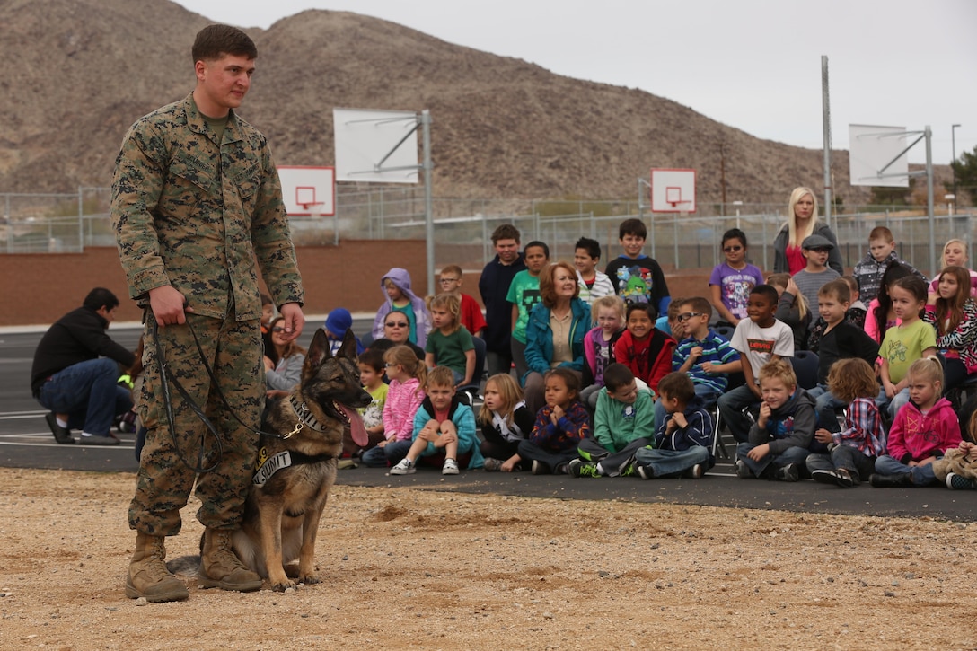 Cpl. John Scudder, military working dog handler, K-9 unit, Provost Marshal’s Office, holds on to Baby, MWD, PMO, before a simulated attack on a perpetrator during a demonstration at Joshua Tree Elementary School, Jan. 29, 2015. Scudder has been working with MWDs for three years. (Official Marine Corps Photo by Lance Cpl. Julio McGraw/ Released)