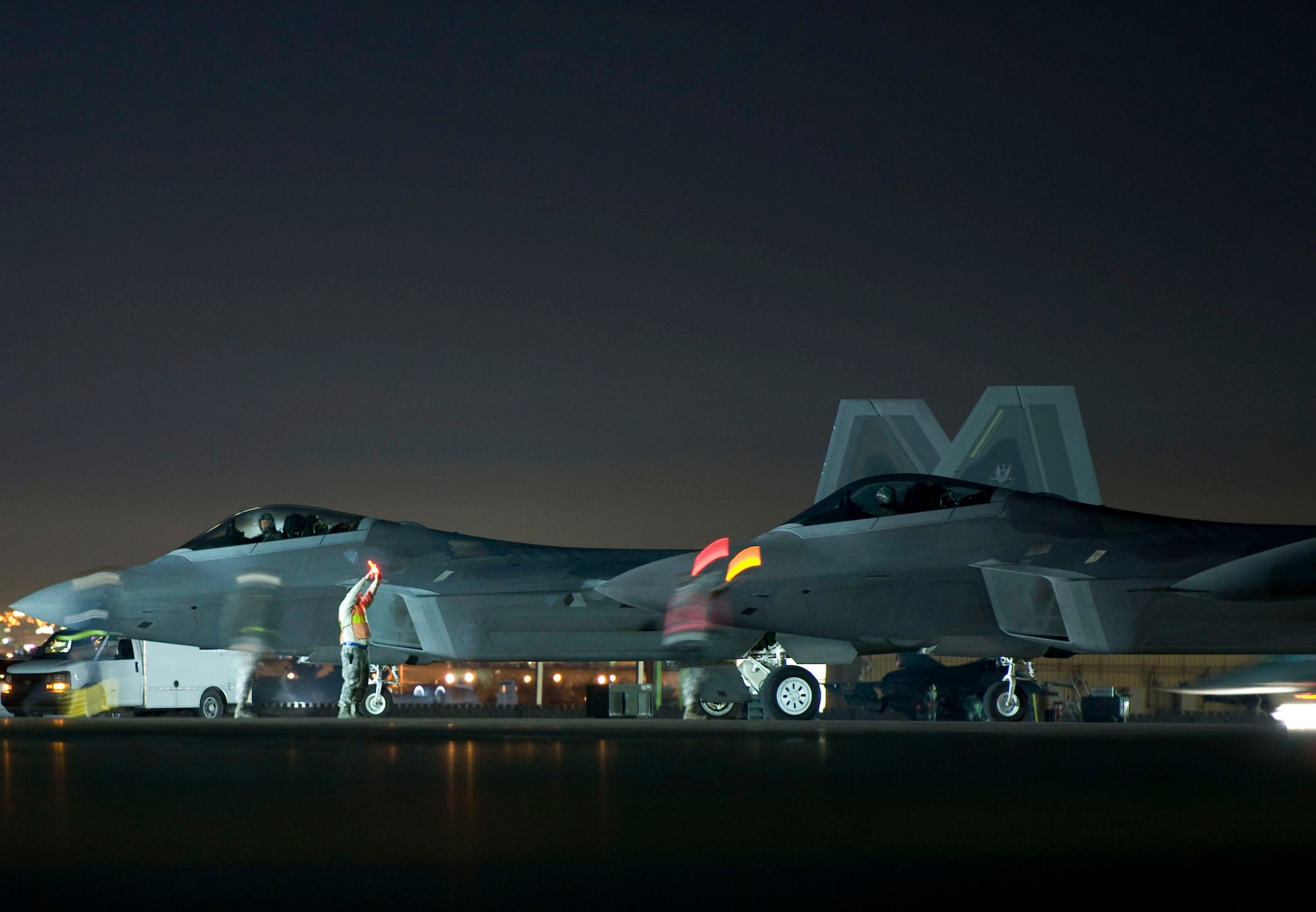 Two crew chiefs marshal two F-22 Raptors assigned to the 94th Fighter Squadron, Joint Base Langley-Eustis, Va., at Nellis Air Force Base, Nev., Feb. 4, 2015. In addition to daytime operations, Red Flag conducts training exercises during the hours of darkness to train for low-visibility environments. (U.S. Air Force photo by Airman 1st Class Mikaley Towle)