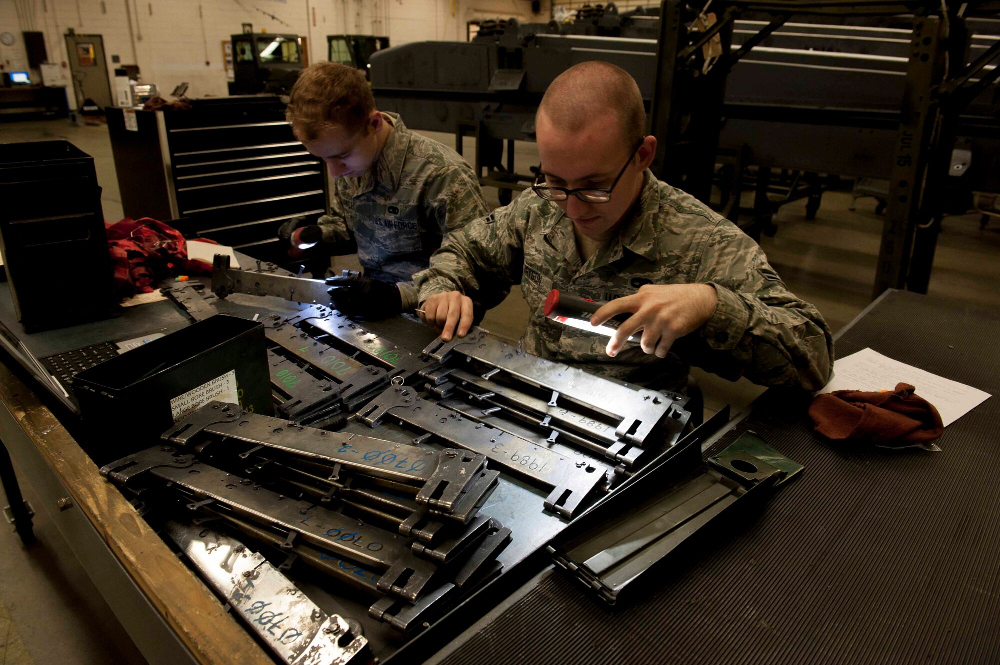 Airman 1st Classes Cody Bryson and Luke Markle, 5th Munitions Squadron armament team members, clean B-11 shackles on Minot Air Force Base, N.D., Feb. 3, 2015. They used small bore brushes to remove rust and debris to ensure the pieces are in proper working order. (U.S. Air Force photo/Airman 1st Class Sahara L. Fales)