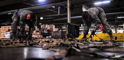 Senior Airman Darwin Polo and Senior Airman Maria Harrison, 88th Aerial Port Squadron air transportation specialists, prepare straps used to secure a pallet Feb. 9, 2015, at the 437th Aerial Port Squadron on Joint Base Charleston, S.C. The “Port Dawgs” work through the night to ensure the safe handling of cargo, for transportation throughout the world.(U.S. Air Force photo/Airman 1st Class Clayton Cupit)