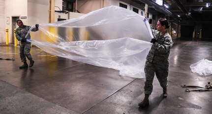 Senior Airman Melissa Howerton and Senior Airmen Darwin Polo, 437th Aerial Port Squadron air transportation specialists, prepare to cover a pallet with a protective sheet Feb. 9, 2015, at Joint Base Charleston, S.C. The need for safe, precise, reliable airlift never stops, and therefore neither do the “Port Dawgs.” They work through the night to process cargo and load it on and off Charleston’s fleet of C-17 Globemaster IIIs.(U.S. Air Force/Airman 1st Class Clayton Cupit)