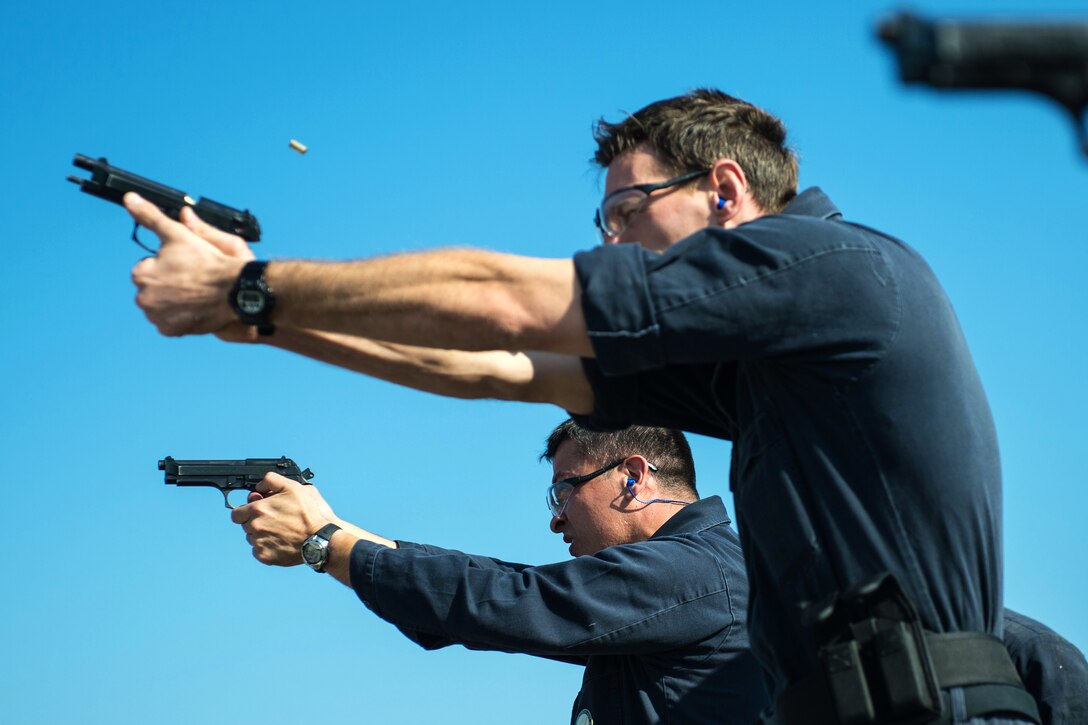 U.S. Navy Petty Officer 1st Class Jorge Delgado, foreground, fires an M9 service pistol during a pistol qualification aboard the guided-missile destroyer USS Mitscher in the U.S. 5th Fleet area of operations, Jan. 29, 2015. Delgado is a Navy counselor.